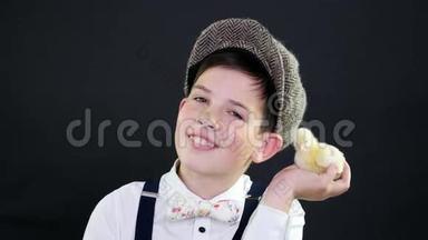 肖像，一个戴着帽子和吊带的漂亮男孩和一只黄色的小鸭子玩.. 专题装饰的工作室视频
